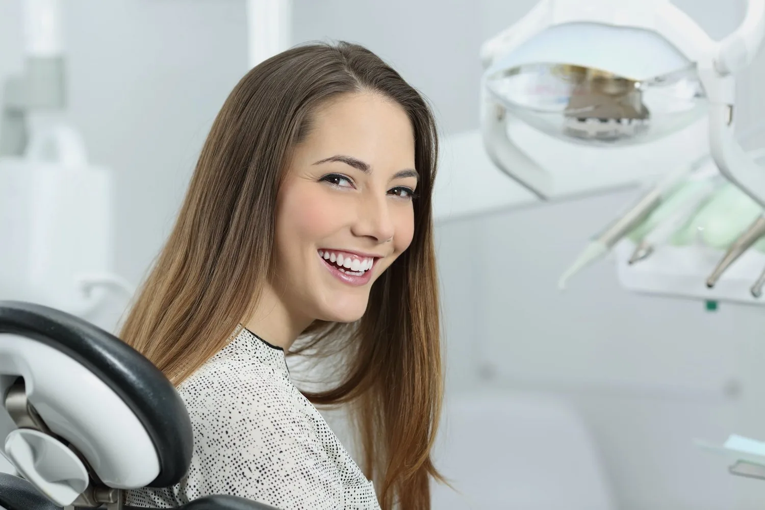 A smiling patient sitting in a dental chair next to dental equipment.